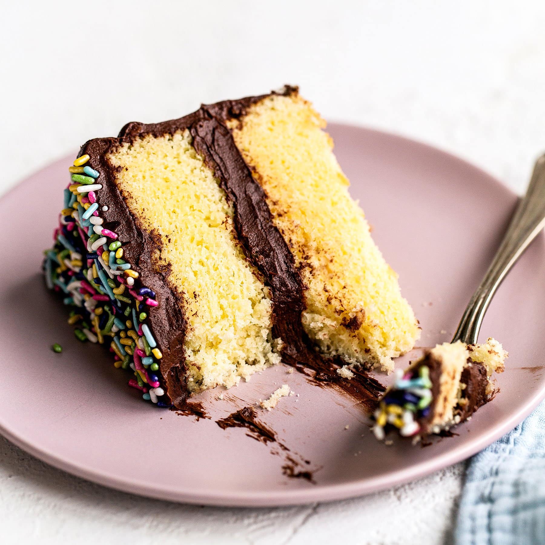 Slice of yellow cake on a plate with a bite taken out with a fork
